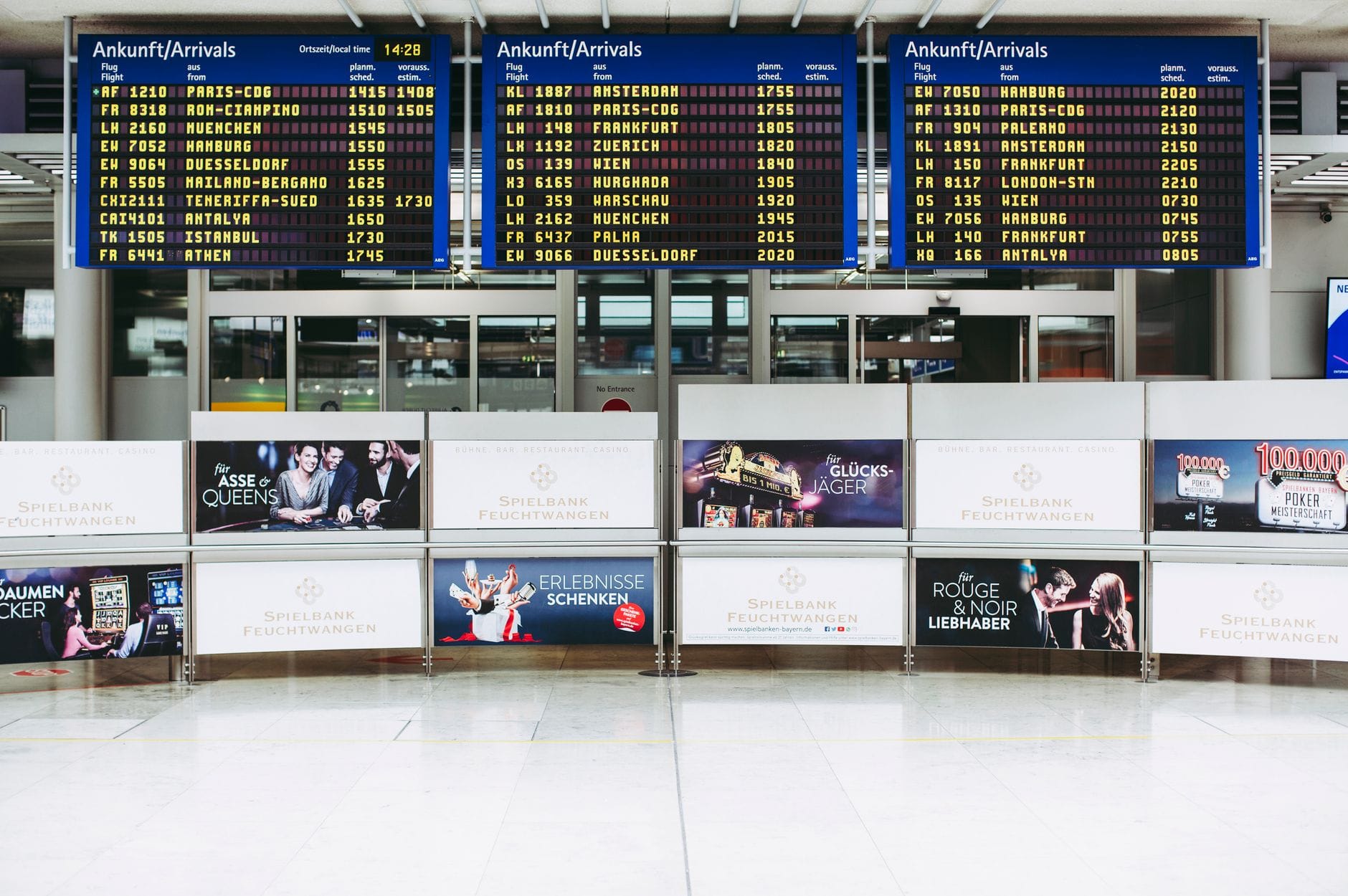 Area arrivi dell'Aeroporto Internazionale di Vienna con tabelloni dei voli in tedesco e area d'attesa visibili.