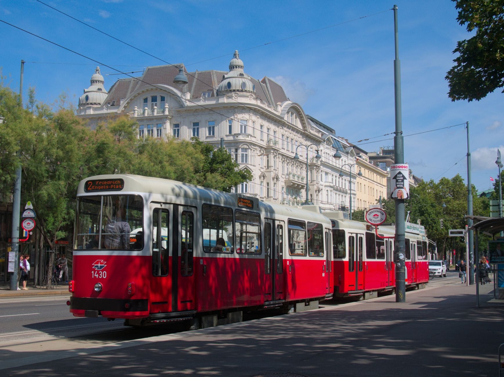 Un classico tram rosso di Vienna davanti a grandi edifici storici, con fili e segnali del tram, in una luminosa giornata di sole.