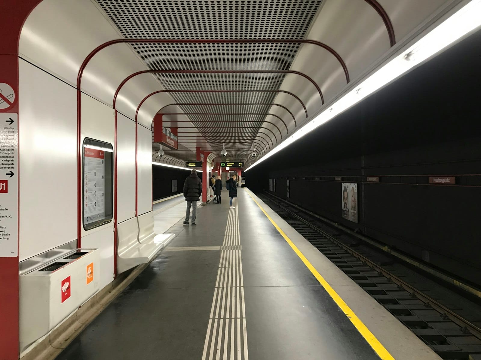 Banchina moderna della metropolitana di Vienna con dettagli rossi, linea di sicurezza gialla e passeggeri in attesa del treno.