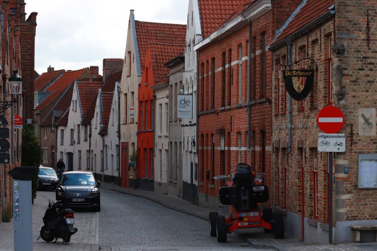 Narrow cobblestone street in Bruges old town with a few parked cars, brick houses, and parking signs visible