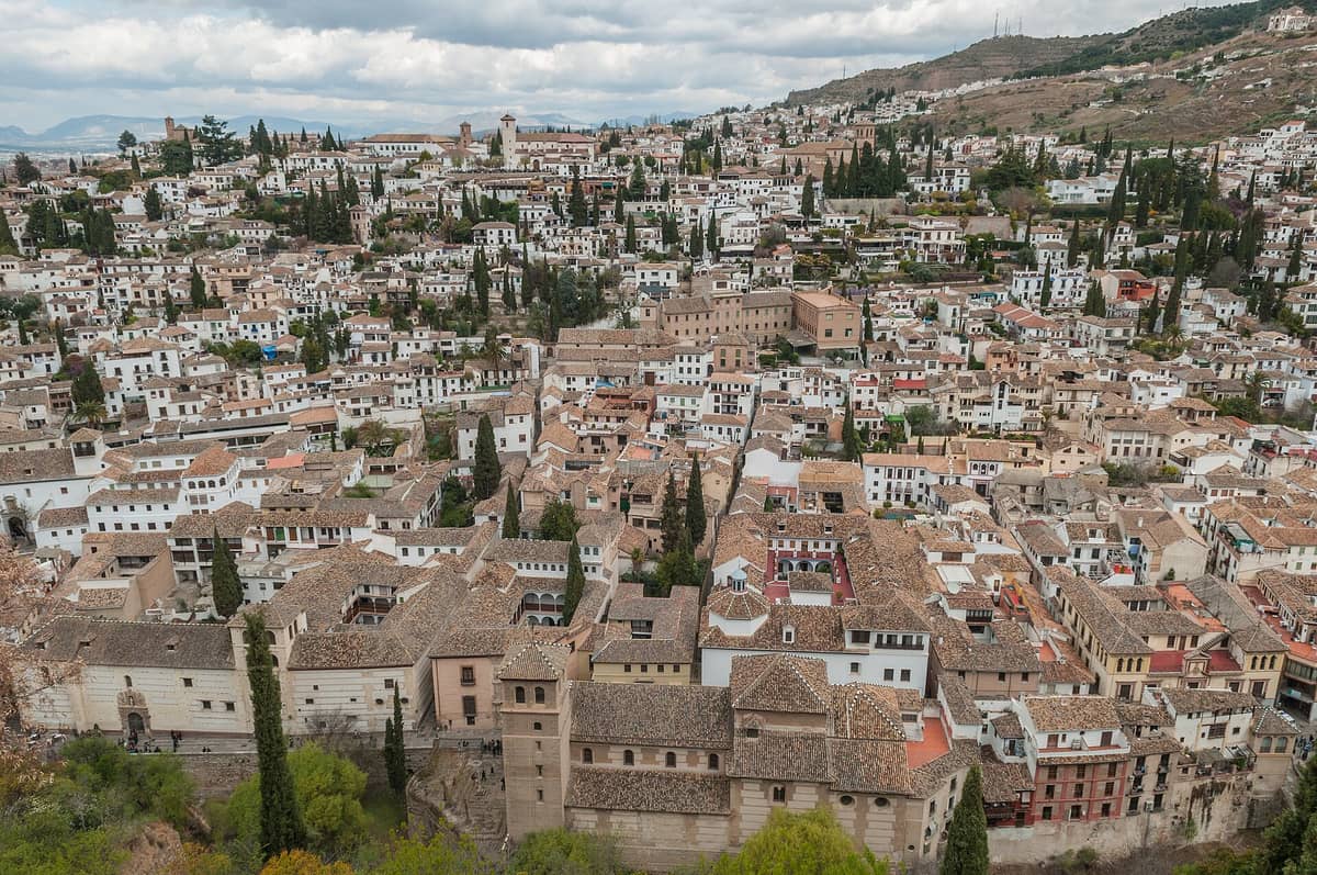 วิวพาโนรามาของย่าน Albaicín ในเมือง Granada พร้อมบ้านสีขาวแบบดั้งเดิม หลังคาดินเผา ต้นไซเปรส และเชิงเขา Sierra Nevada โดยรอบ