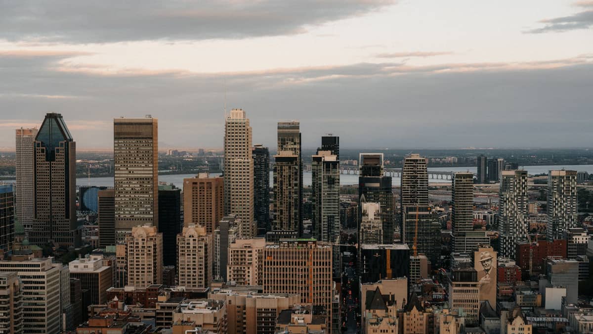 Panoramablick auf die Skyline der Innenstadt von Montreal mit hohen Bürotürmen und Stadtlichtern unter einem teilweise bewölkten Abendhimmel.