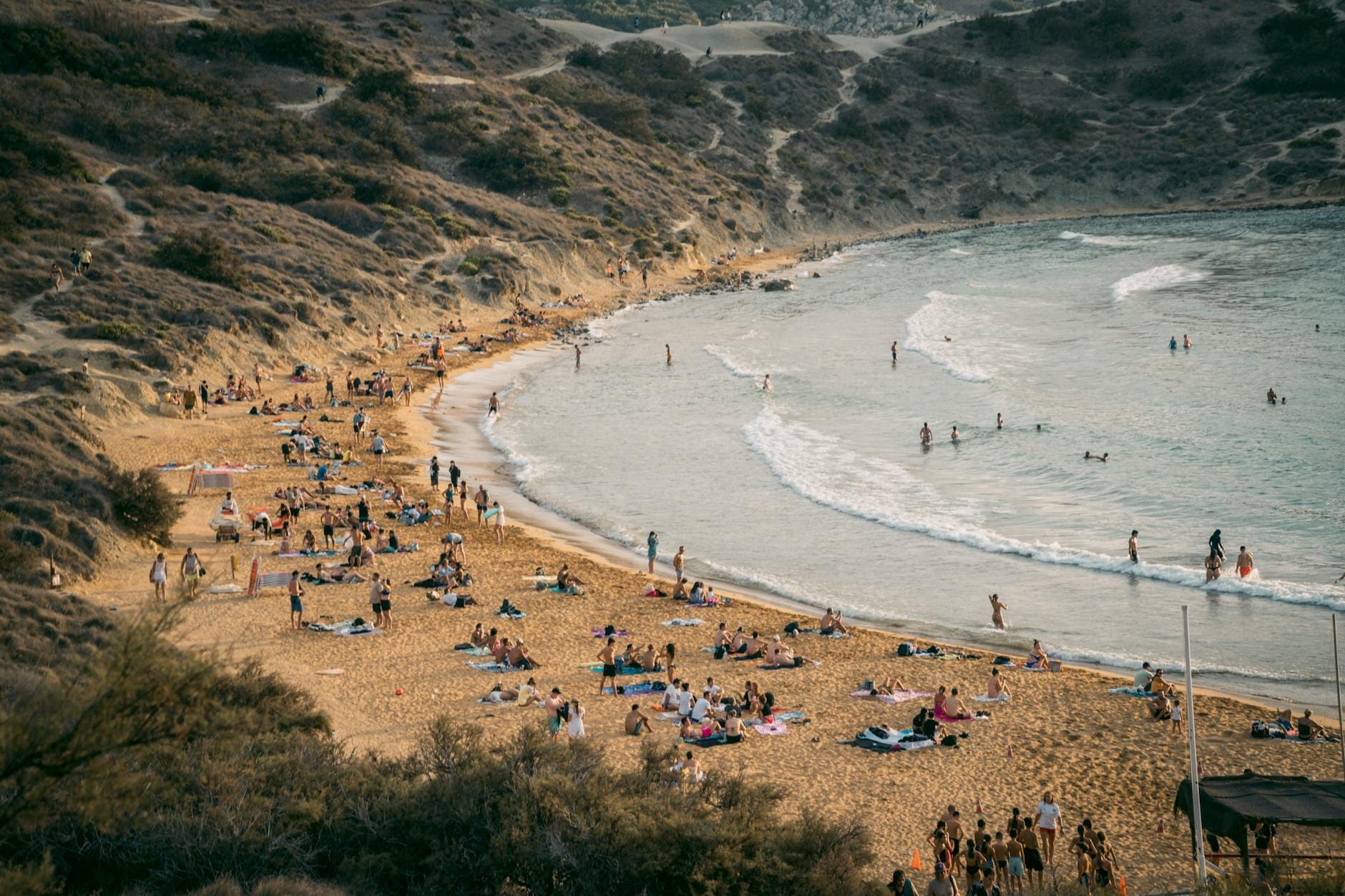 Un'ampia spiaggia sabbiosa ai piedi di scogliere verdi, con persone che si rilassano e nuotano, onde gentili e un ambiente naturale incontaminato a Għajn Tuffieħa Bay.