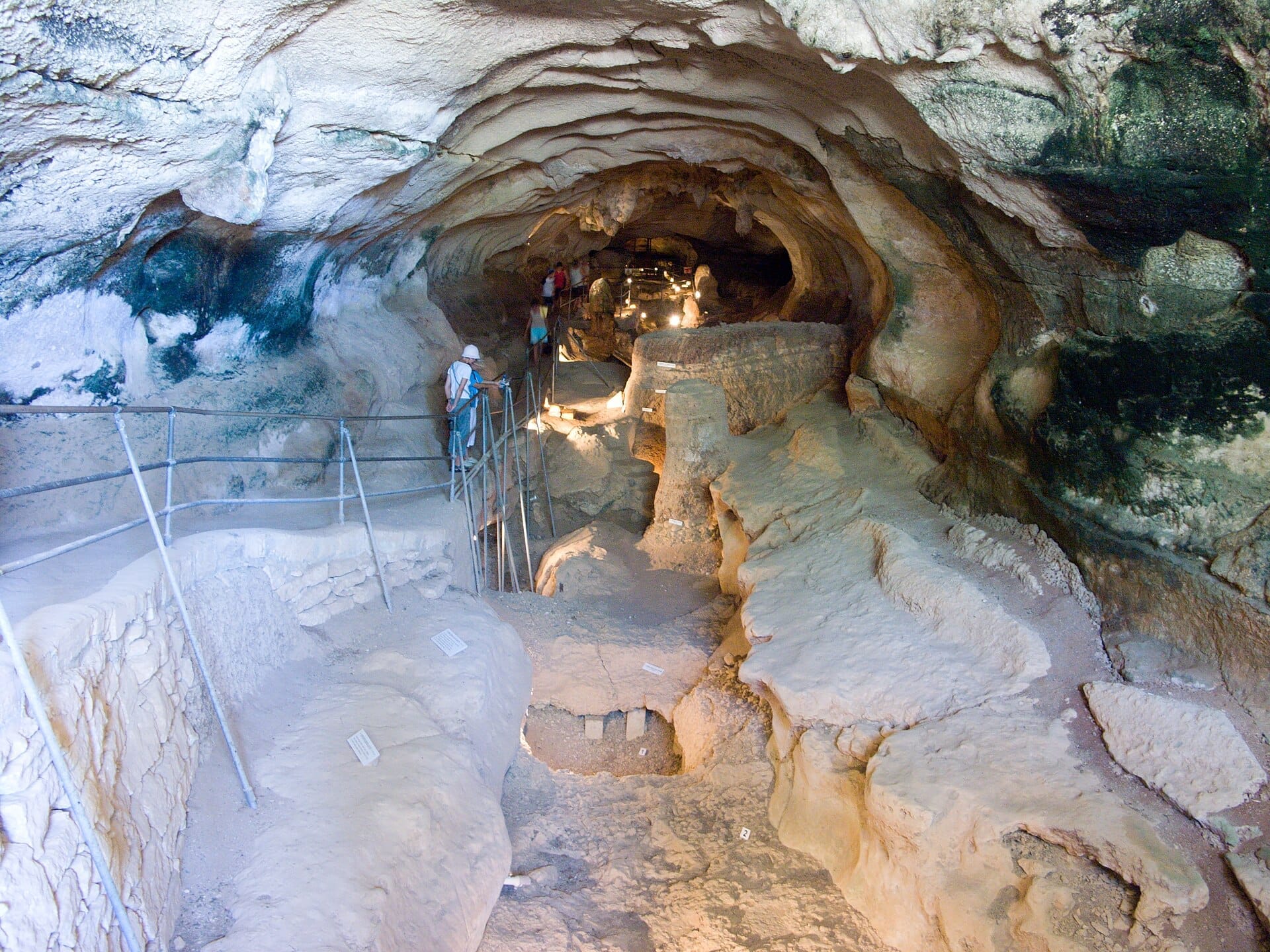 I visitatori esplorano il corridoio interno illuminato della Grotta Għar Dalam a Malta, circondato da aspre formazioni rocciose e antichi strati geologici.