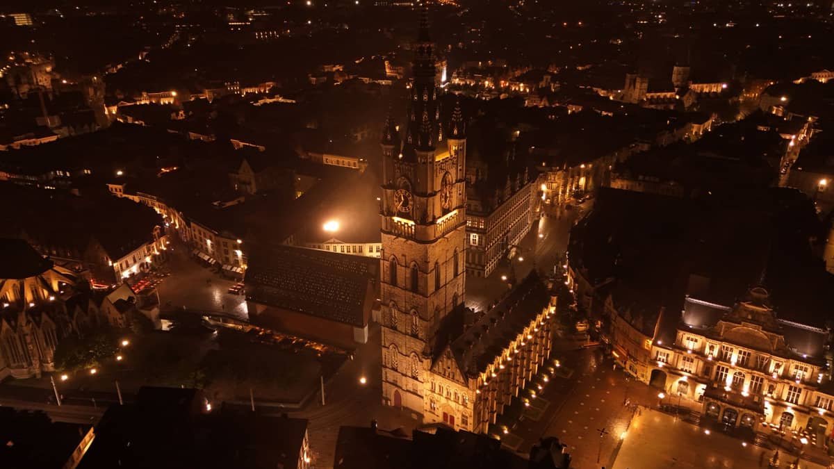 Aerial night view of Sint-Baafsplein square in Ghent with St Bavo’s Cathedral and the Belfry, illuminated by warm lights.