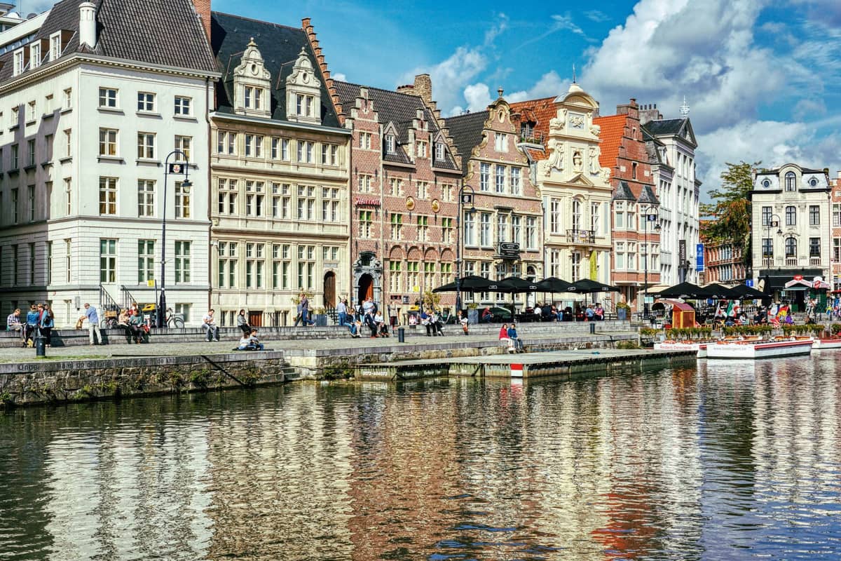 Waterfront of historic Ghent lined with outdoor seating, cafes, and restaurants beneath ornate Flemish buildings on a sunny day.