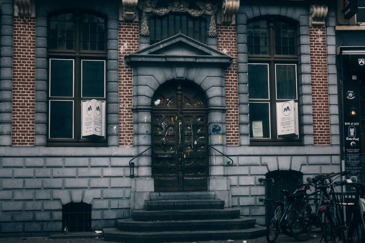 Front entrance of a hostel building in Ghent with bicycles parked outside and hostel signage in the windows.