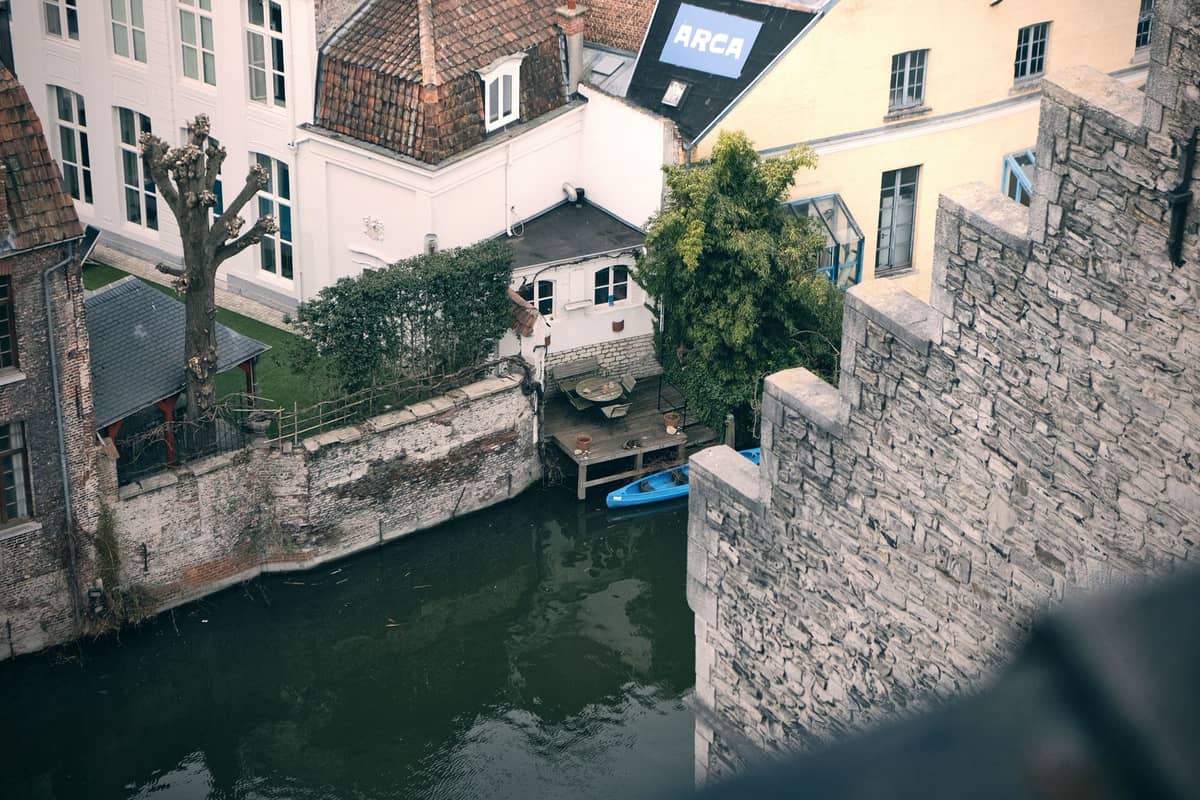 Atmospheric view of a hidden canal-side courtyard in Ghent, with garden, boats, and old brick and stone walls.