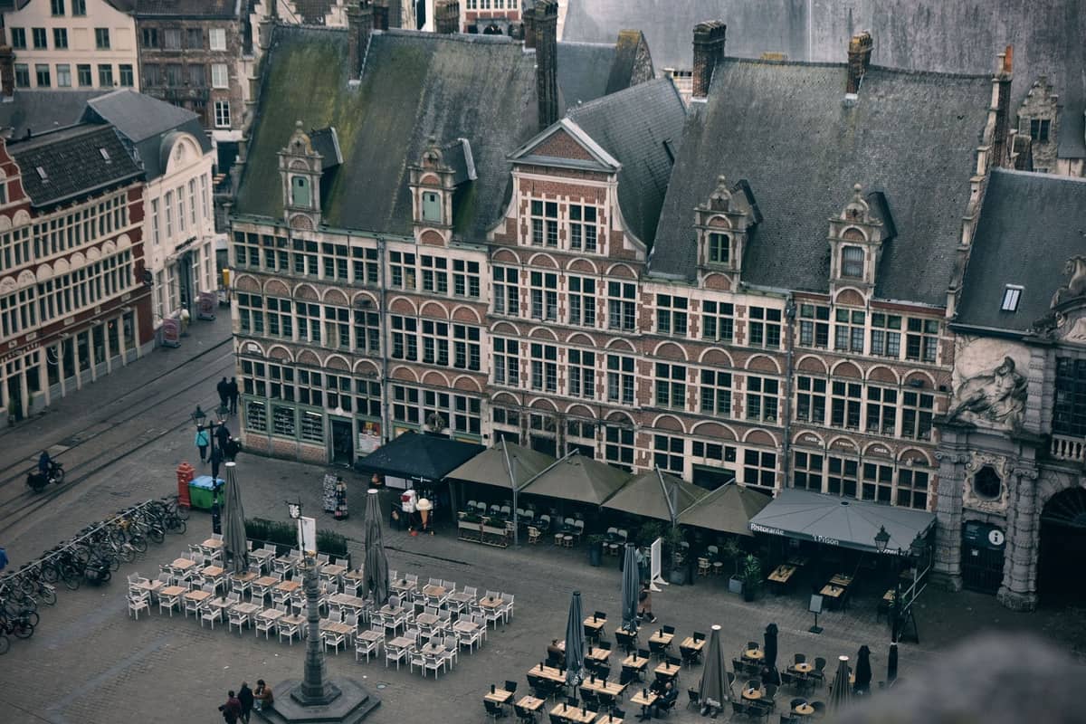 Overhead view of a historic square in Ghent with outdoor café seating, ornate Flemish buildings, and people socializing.