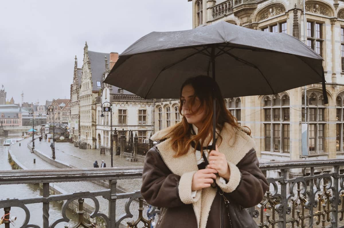 Woman holding an umbrella on a rainy day in Ghent with classic city architecture and wet cobblestone streets in the background