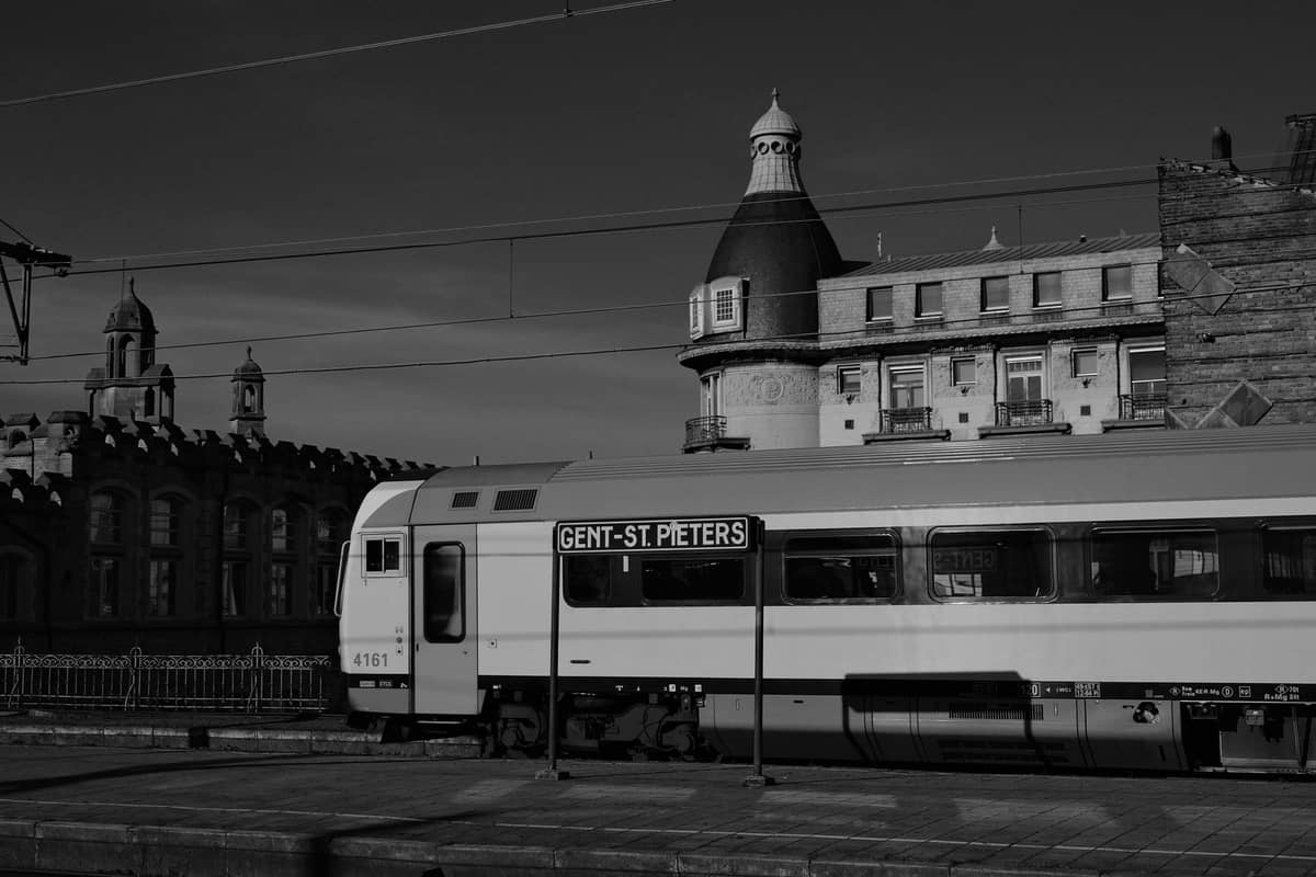 Black and white photo of a train at Gent-Sint-Pieters station with historic buildings in the background and a platform sign.