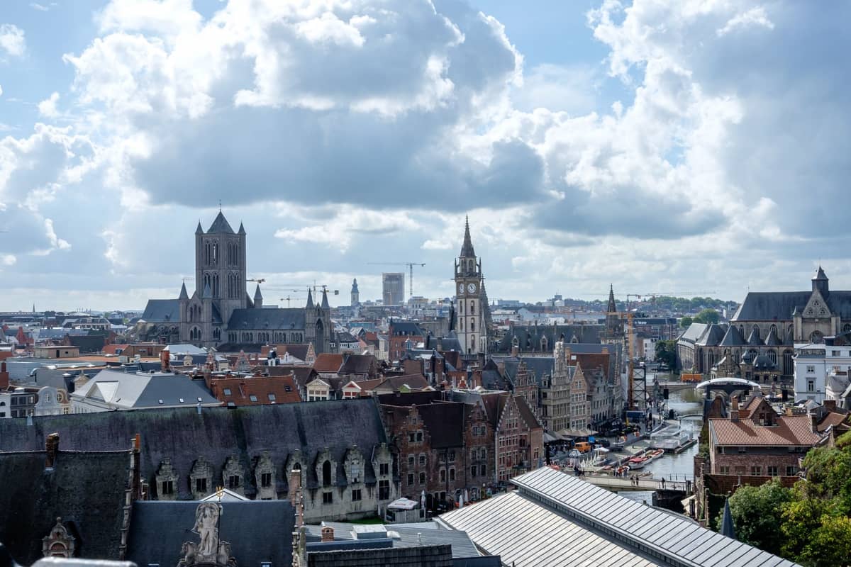 Panoramic cityscape view of Ghent featuring St. Nicholas' Church, the Belfry, and St. Bavo's Cathedral with distinctive medieval towers, seen from above on a clear day.