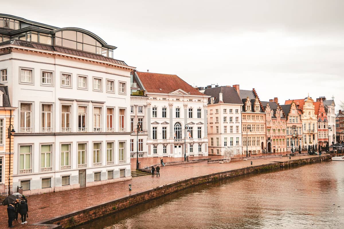 Canal-side view of historic Ghent buildings with people strolling along the quays on an overcast day