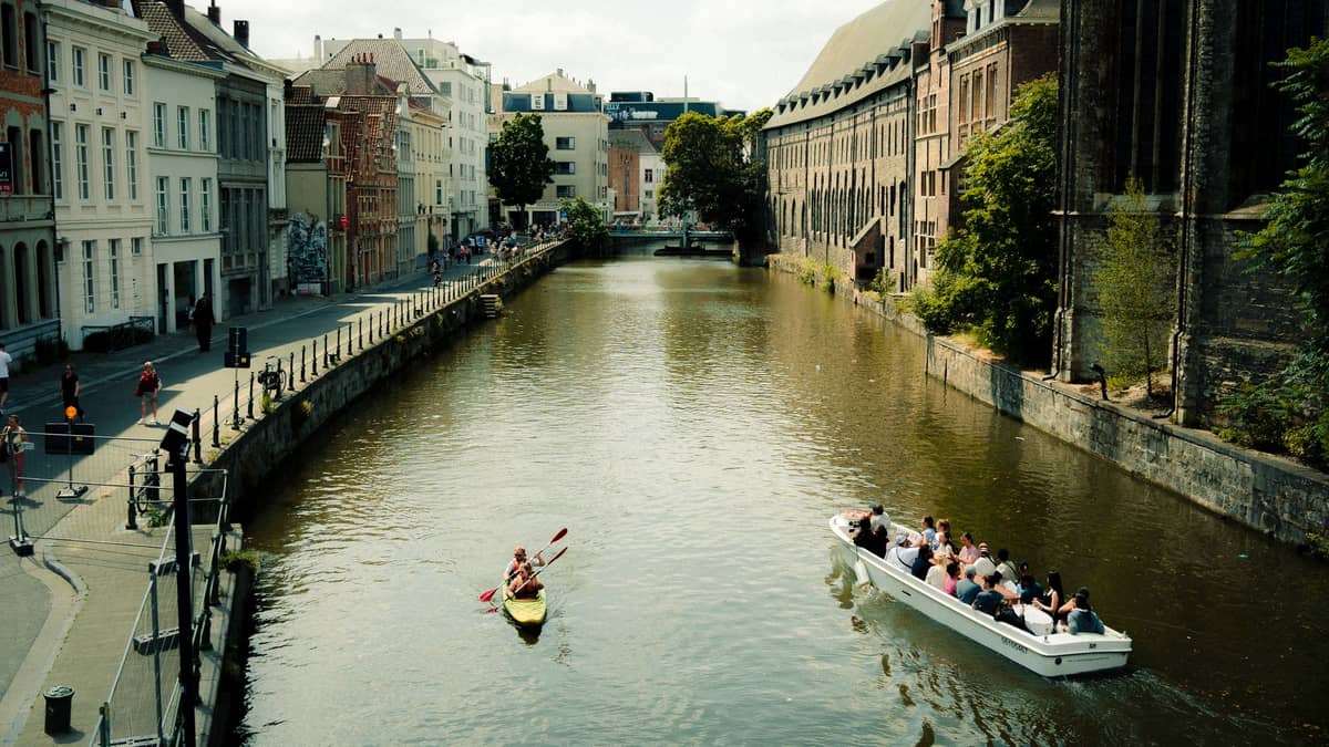 View of Ghent canal with people kayaking and boat tour, historic buildings line both sides of the waterway