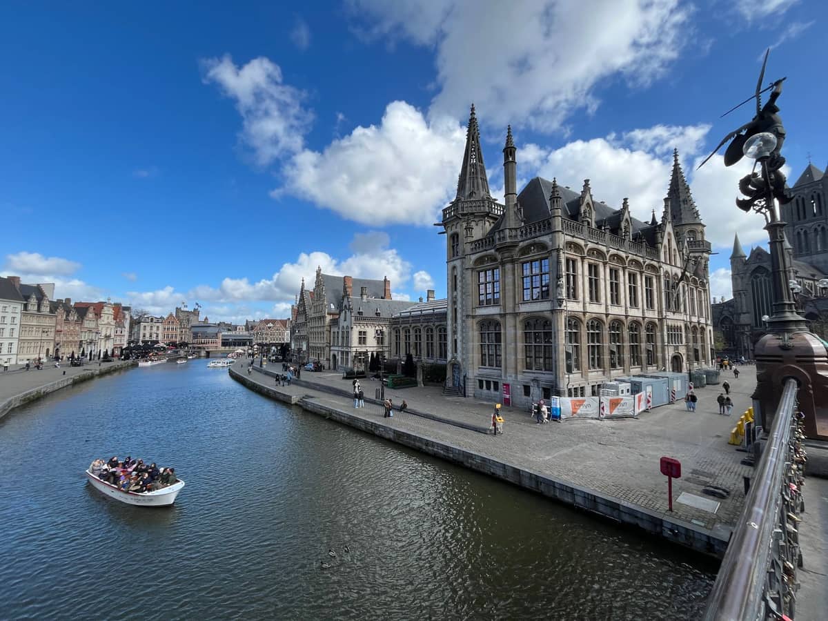 Wide view of Ghent’s historic canal with children and adults enjoying a boat tour, surrounded by beautiful medieval buildings and blue sky.