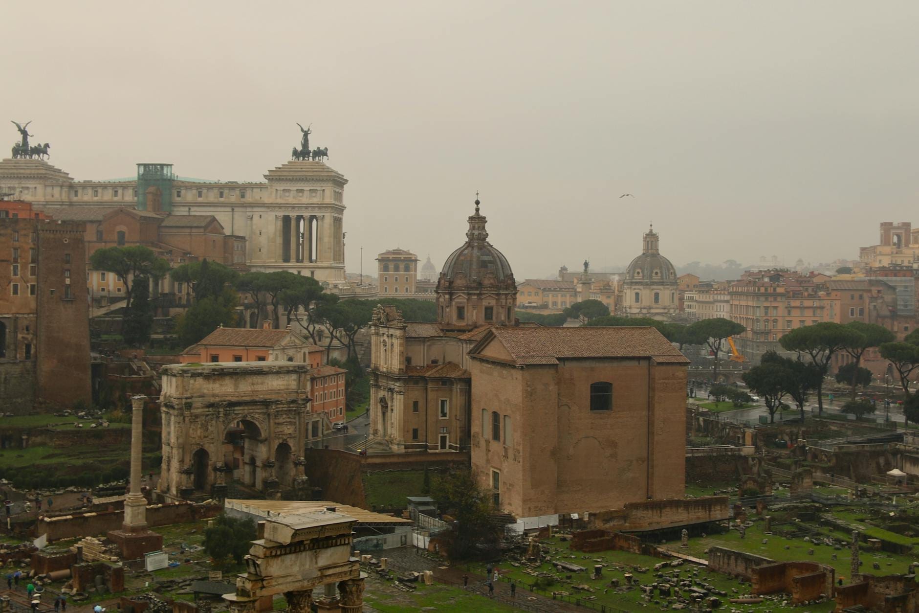 Panoramic view from Gianicolo Hill featuring Rome’s skyline, ancient ruins, church domes, and the Vittoriano monument under cloudy skies.
