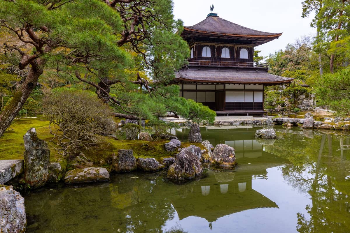 The Silver Pavilion (Ginkaku-ji) in Kyoto, framed by lush green trees and reflected in a tranquil pond in the foreground.
