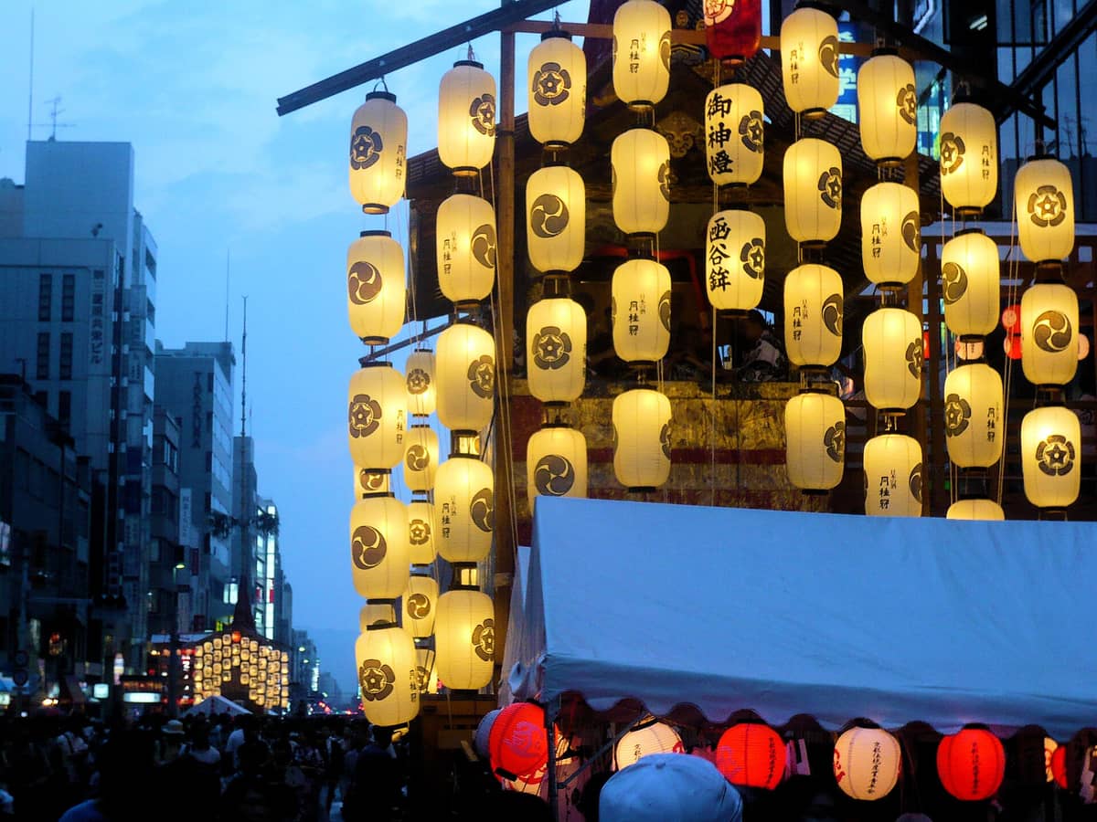 Crowds gather in downtown Kyoto as illuminated festival lanterns adorn large yamaboko floats during Gion Matsuri night festivities.