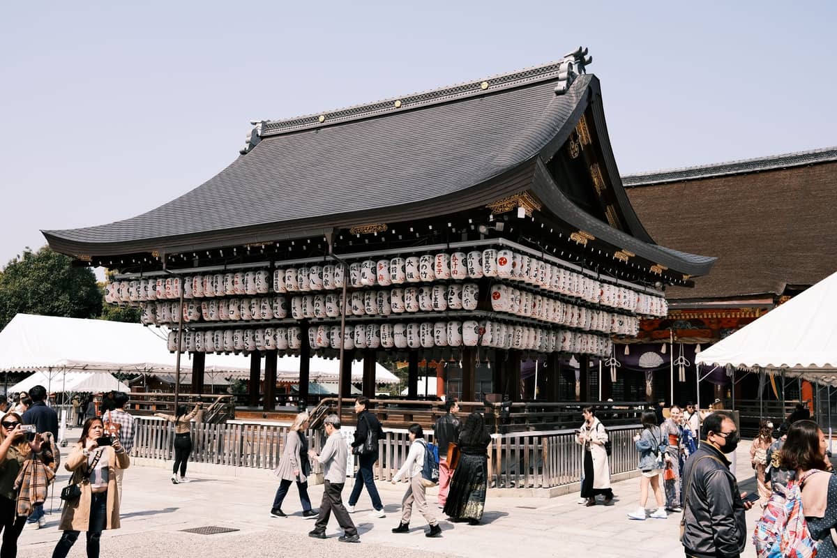 Daytime view of Yasaka Shrine’s main stage adorned with traditional lanterns, with crowds walking around during festival season in Kyoto.