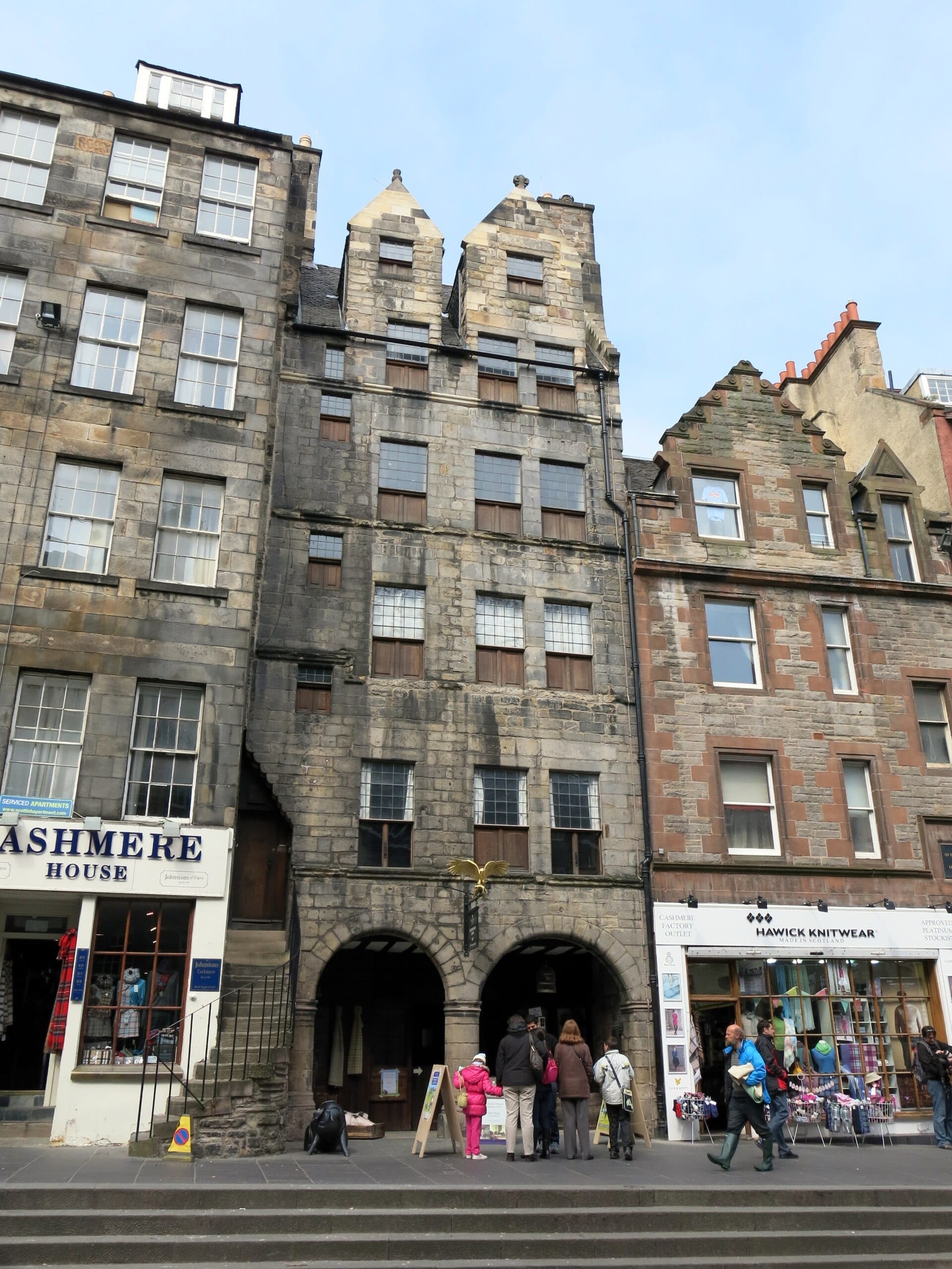 Gladstone's Land, ein hohes steinernes Mietshaus aus dem 17. Jahrhundert mit Bogeneingängen, liegt an der Royal Mile in Edinburgh, umgeben von benachbarten Geschäften und Besuchern.