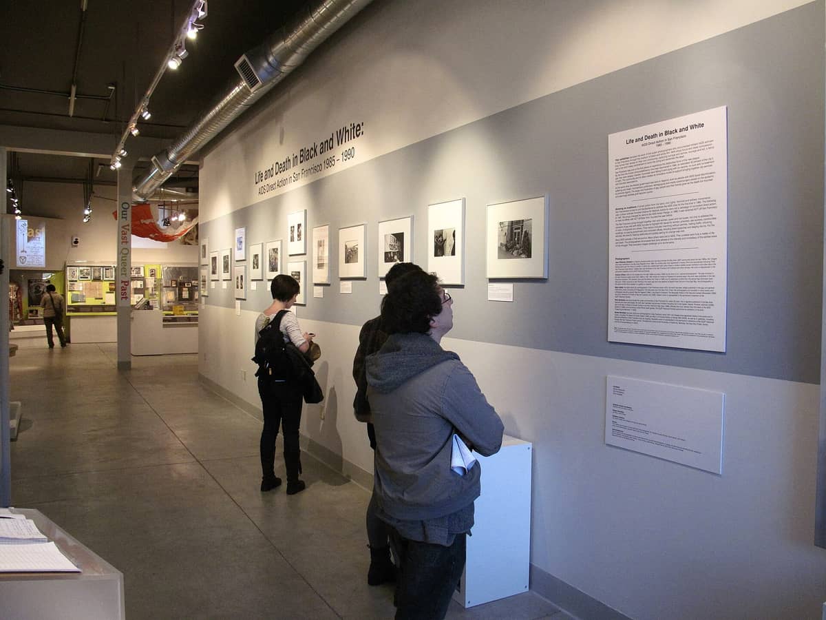 Vista interior del Museo de la Sociedad Histórica GLBT con visitantes observando fotografías enmarcadas y paneles de exposición en una sala bien iluminada.