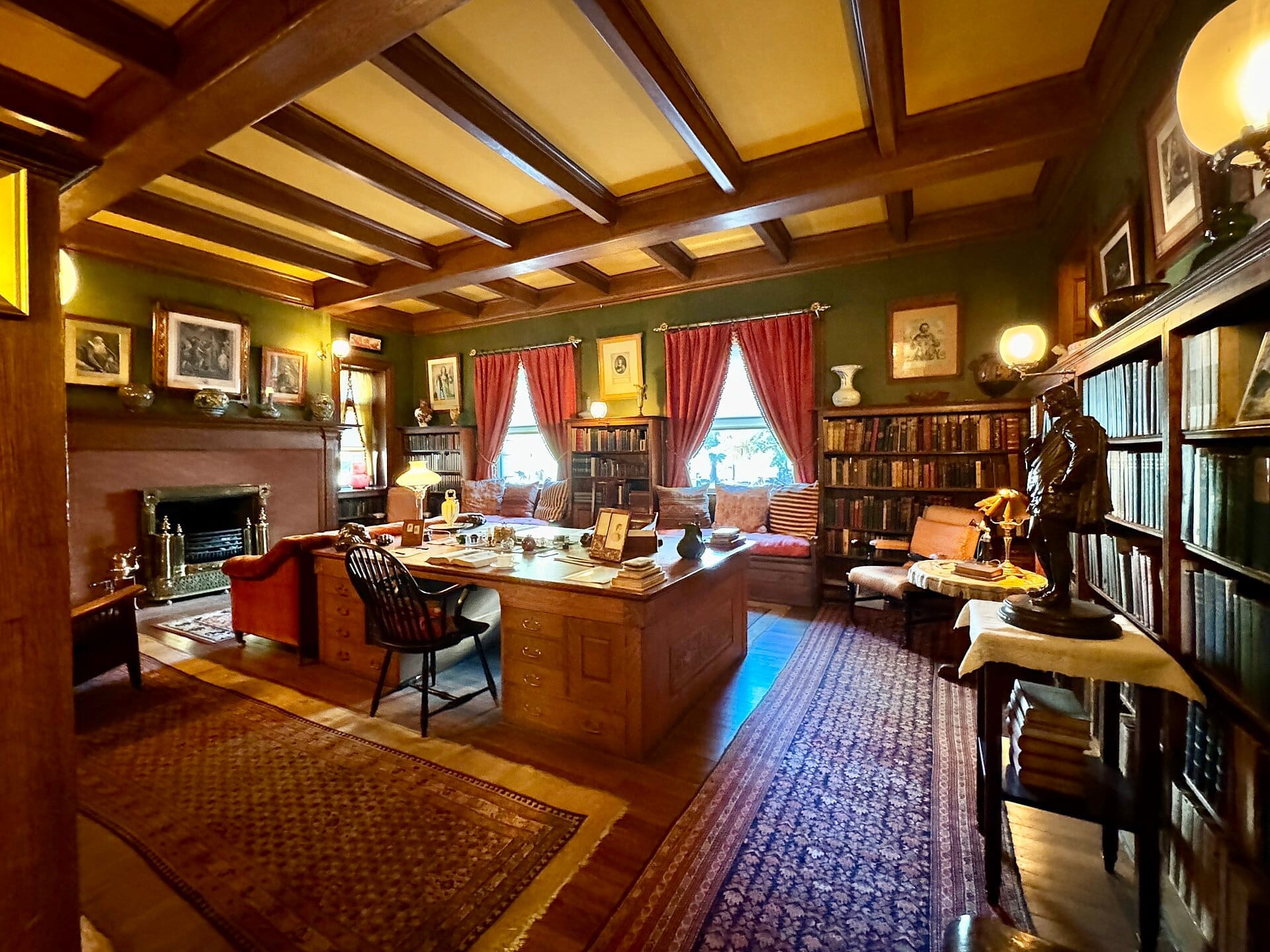 Sala studio storica al Glessner House Museum con soffitto a travi in legno, scrivania vintage, camino, librerie, opere d'arte incorniciate e finestre con drappi rossi.