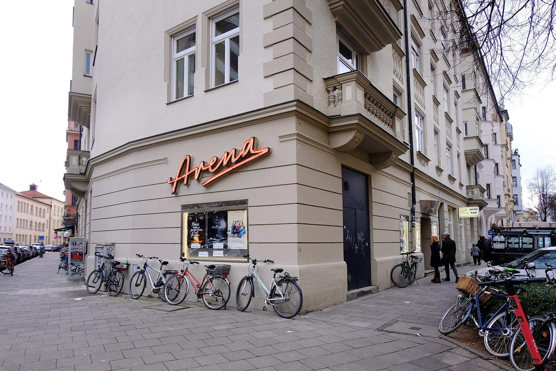 บรรยากาศริมถนนใน Glockenbachviertel มิวนิก ตึกมุมถนนมีป้ายไฟ Arena จักรยานจอด และผู้คนเดินเล่นบนทางเท้า