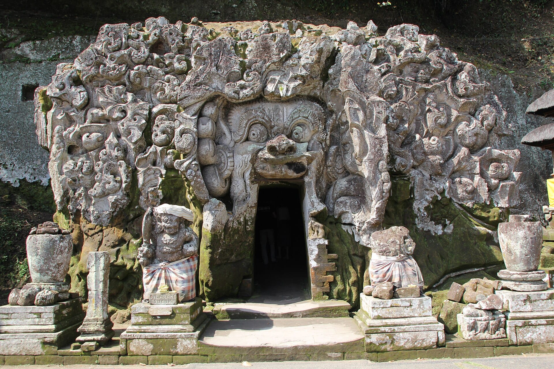 Elaborate sculture in pietra di demoni e creature mitiche adornano il minaccioso ingresso della Grotta dell'Elefante Goa Gajah a Bali.