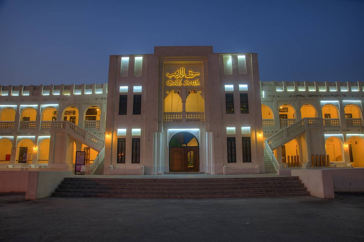 Haupteingang des Doha Gold Souq in der Abenddämmerung beleuchtet, mit traditioneller Architektur aus Bögen, Balkonen und sanftem gelbem Licht.