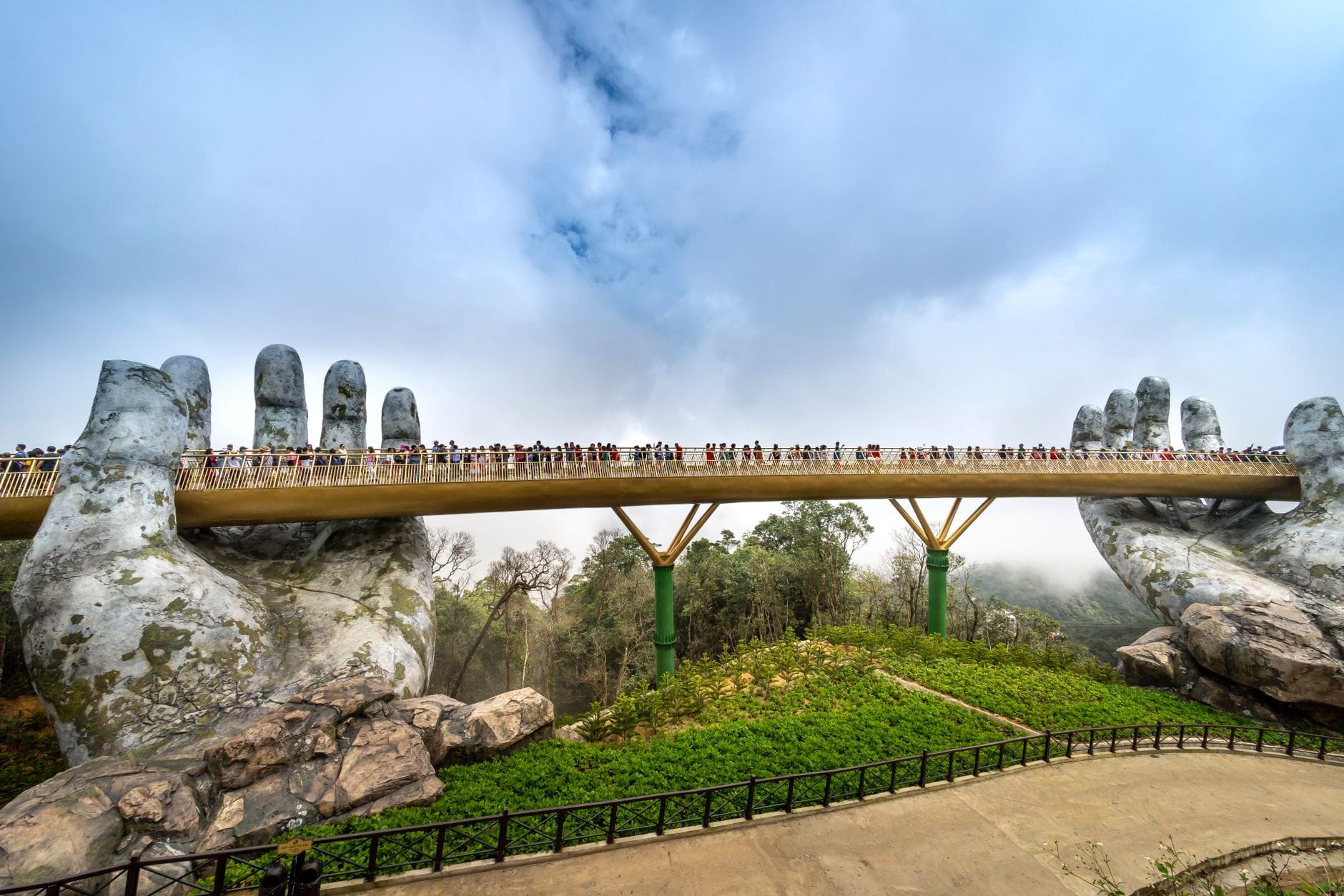 สะพานทองใจกลางบานาฮิลส์ ดานัง เวียดนาม สะพานโค้งสีทองยาวเหนือขุนเขา มือหินยักษ์อุ้มไว้ รายล้อมด้วยต้นไม้และหมอกภูเขา