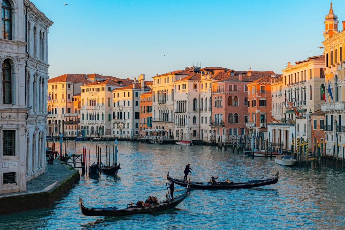 Gondeln auf dem Canal Grande in Venedig zur goldenen Stunde mit Sonnenlicht auf historischen Gebäuden und ruhigem Wasser.