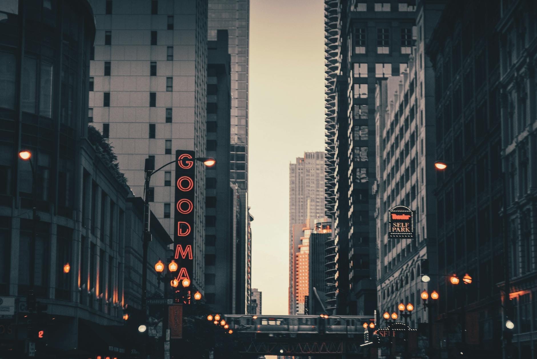 Veduta di una strada di Chicago con l'insegna al neon verticale illuminata del Goodman Theatre, circondata dai grattacieli della città e dai lampioni serali.