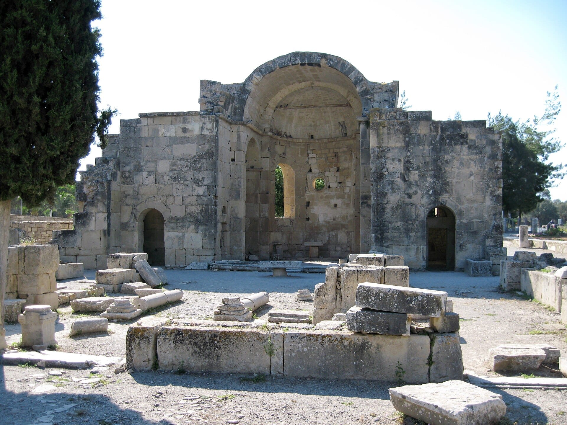 Rovine dell'antica basilica di Gortyna a Creta, con mura in pietra consumate, colonne sparse e brillante luce solare di mezzogiorno.