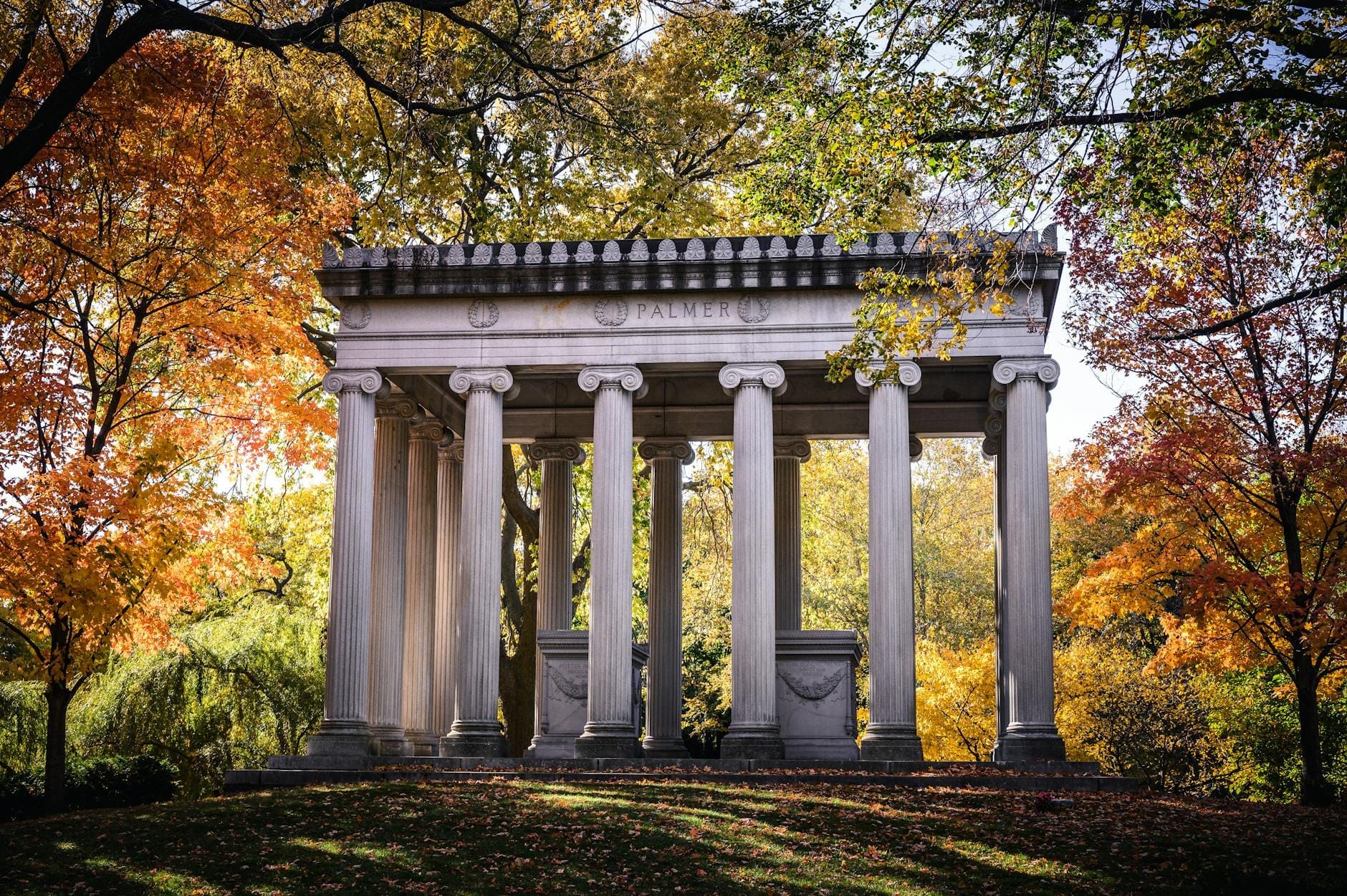Maestoso mausoleo neoclassico circondato da alberi dai colori autunnali nel Cimitero di Graceland, tra architettura storica e un'atmosfera serena da arboreto.