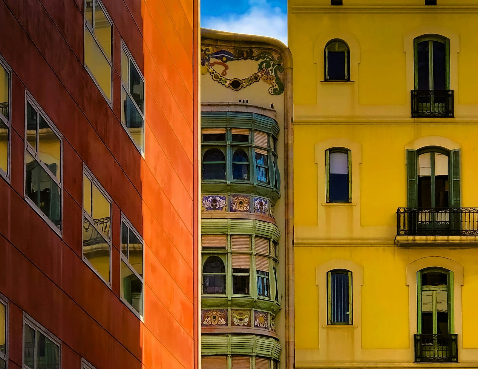 Colorful close-up view of Gràcia’s buildings, featuring vibrant yellow and orange facades, ornate balconies, and detailed windows under a blue sky.