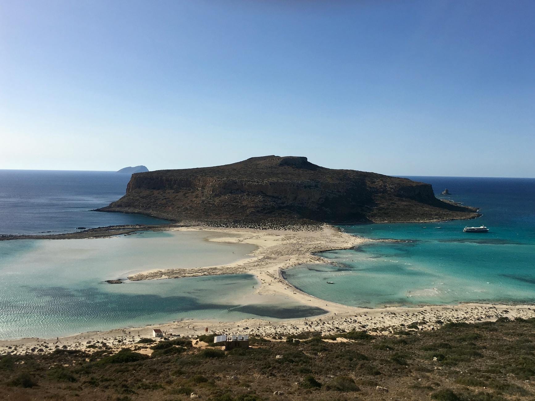 Vista dell'isola di Gramvousa con le sue scogliere frastagliate, acque turchesi cristalline, spiaggia di sabbia e una barca ancorata al largo sotto un cielo azzurro.