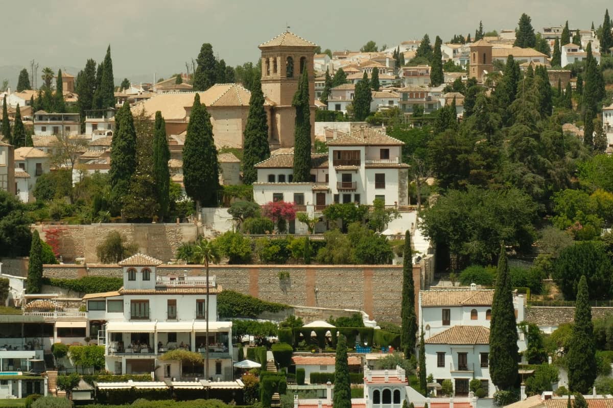 วิวย่าน Albaicín ในเมือง Granada ที่มีบ้านฉาบปูนสีขาว ต้นไซเปรสเขียวชอุ่ม และหอระฆังโบสถ์เก่าแก่ที่โดดเด่นเหนือบ้านเรือนดั้งเดิมบนเนินเขา