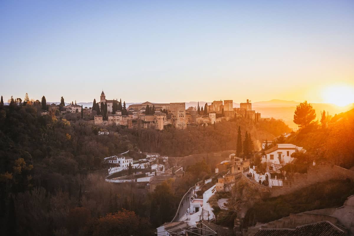 วิวทิวทัศน์จากยอดเขามองลงมายัง Granada ในยามพระอาทิตย์ตก เห็น Alhambra และบ้านฉาบปูนขาวด้านล่าง พร้อมเนินเขาลูกคลื่นในฉากหลัง