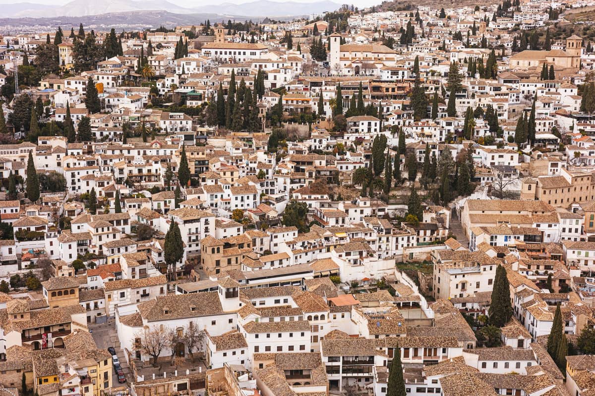 วิวกว้างของย่าน Albaicín ในเมือง Granada พร้อมอาคารสีขาวฉาบปูน หลังคาดินเผา และต้นไซเปรสบนเนินเขา ใต้ท้องฟ้าฤดูหนาวที่มีเมฆปกคลุม