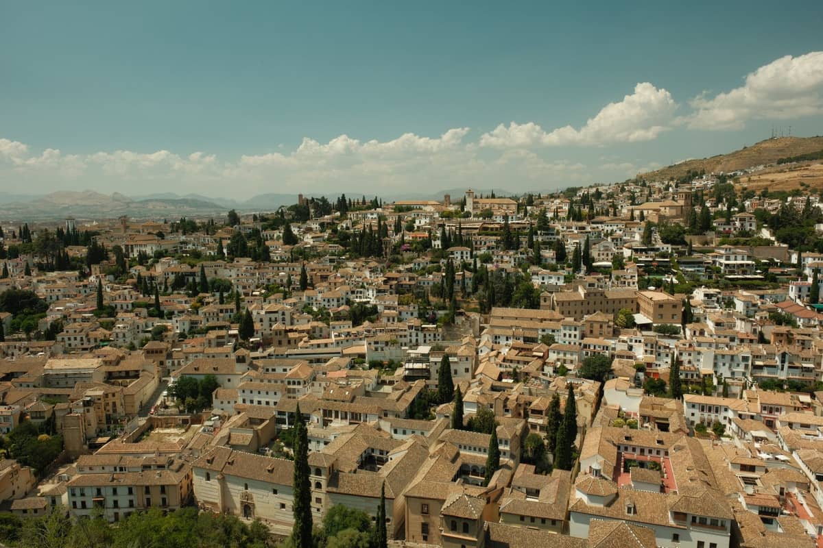 วิวกว้างที่สดใสของย่าน Albaicín ในเมือง Granada พร้อมอาคารสีขาวหนาแน่นจากยุคมัวร์ ต้นไซเปรส และเนินเขาในพื้นหลัง