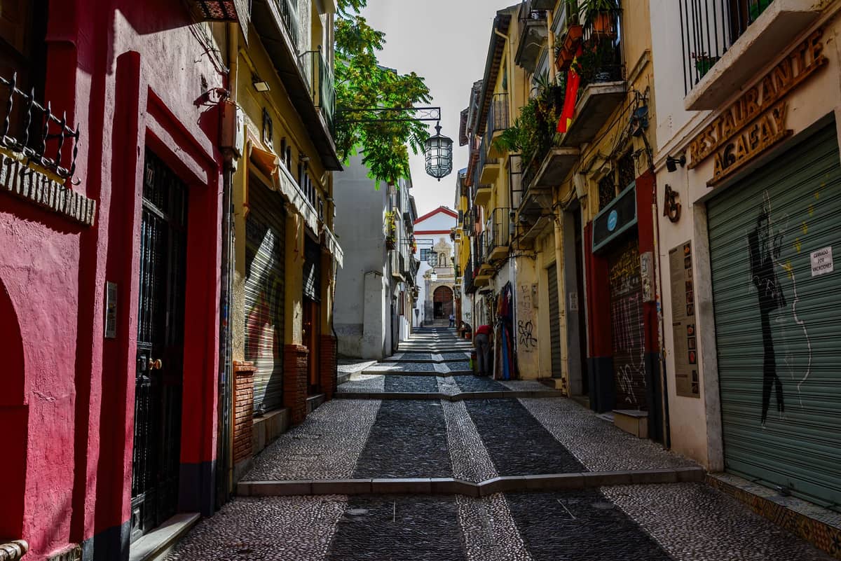 ถนนแคบปูหินในย่านเมืองเก่าของ Granada ที่เรียงรายไปด้วยอาคารสีสันสดใส บาร์ และหน้าร้านที่ปิดบานเกล็ด เหมาะสำหรับการสำรวจย่านชีวิตยามราตรี