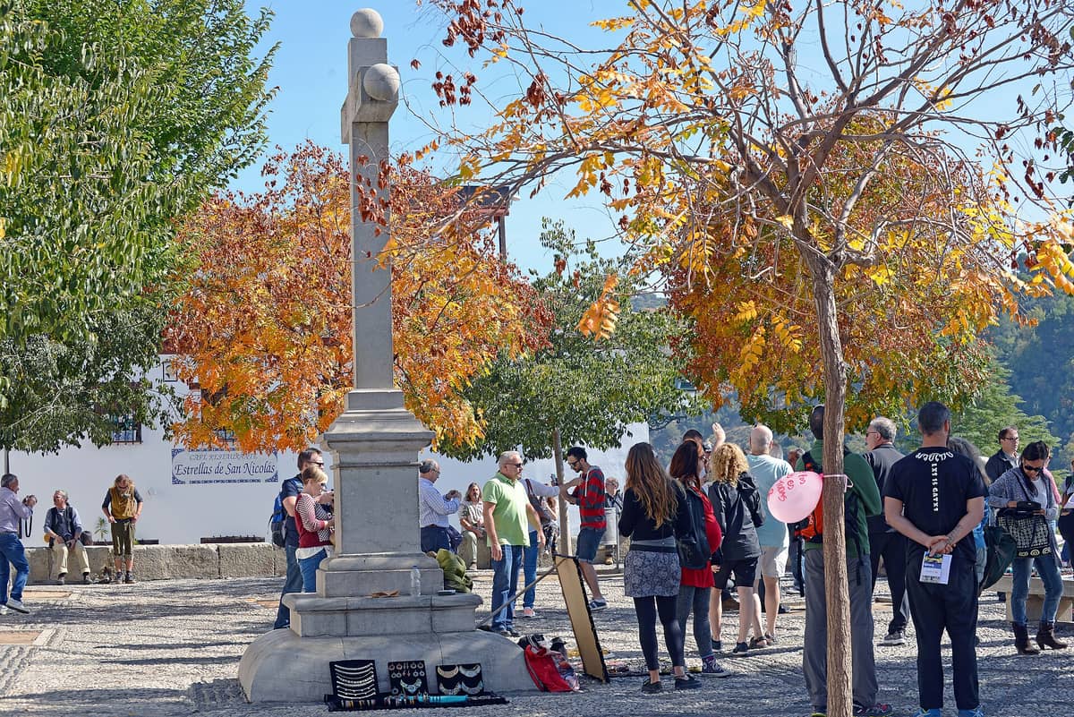 Plaza Mirador de San Nicolás ใน Albaicín เมือง Granada พร้อมนักท่องเที่ยวที่เพลิดเพลินกับลานกว้างและต้นไม้สีสันแห่งฤดูใบไม้ร่วง