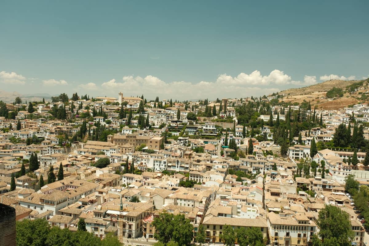 วิวภูมิทัศน์กว้างของย่าน Albaicín และ Realejo ในเมือง Granada พร้อมกลุ่มอาคารสีขาวและต้นไซเปรสใต้ท้องฟ้าสีฟ้า