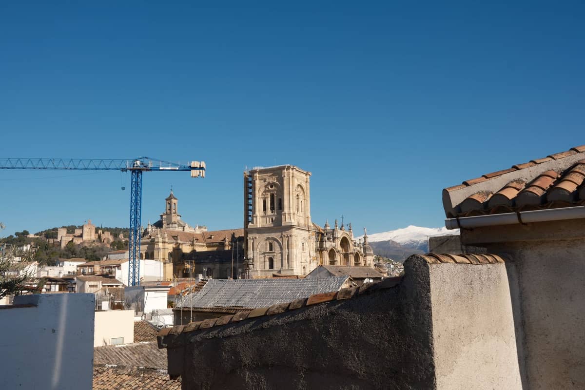 วิวของมหาวิหาร Granada และอาคารประวัติศาสตร์พร้อมหลังคาในเบื้องหน้า เครนก่อสร้าง และเทือกเขา Sierra Nevada ในระยะไกล