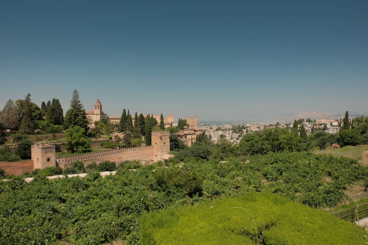 วิวพาโนรามาของกลุ่มอาคาร Alhambra พร้อมหอคอยและพืชพรรณเขียวชอุ่ม มองเห็นเมือง Granada ภายใต้ท้องฟ้าสีฟ้าใส