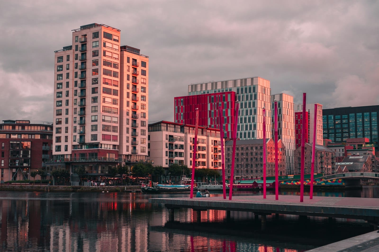 Il Grand Canal Dock al tramonto, con i caratteristici pali rossi, edifici moderni in vetro e i loro riflessi nell'acqua sotto un cielo spettacolare a Dublino.