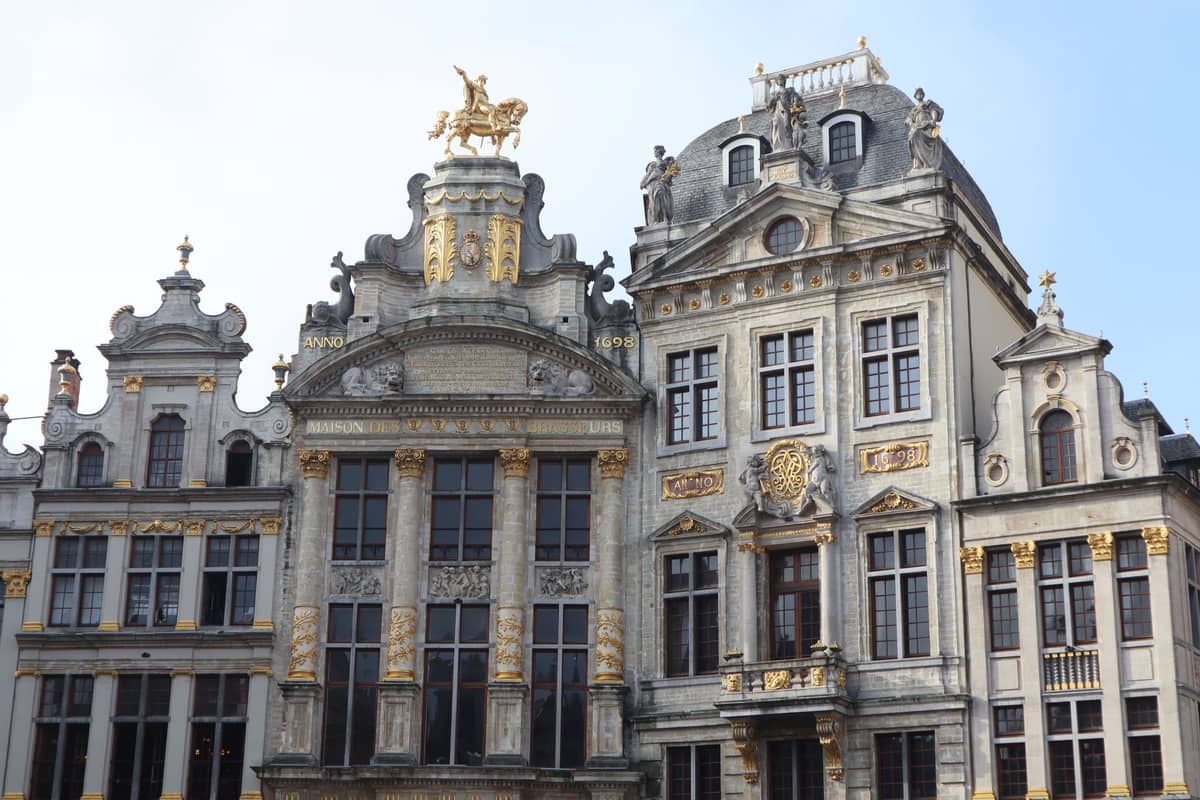 Fachadas clássicas das ornamentadas casas de guildas da Grand-Place, em Bruxelas, com detalhes dourados e arquitetura imponente sob um céu azul.