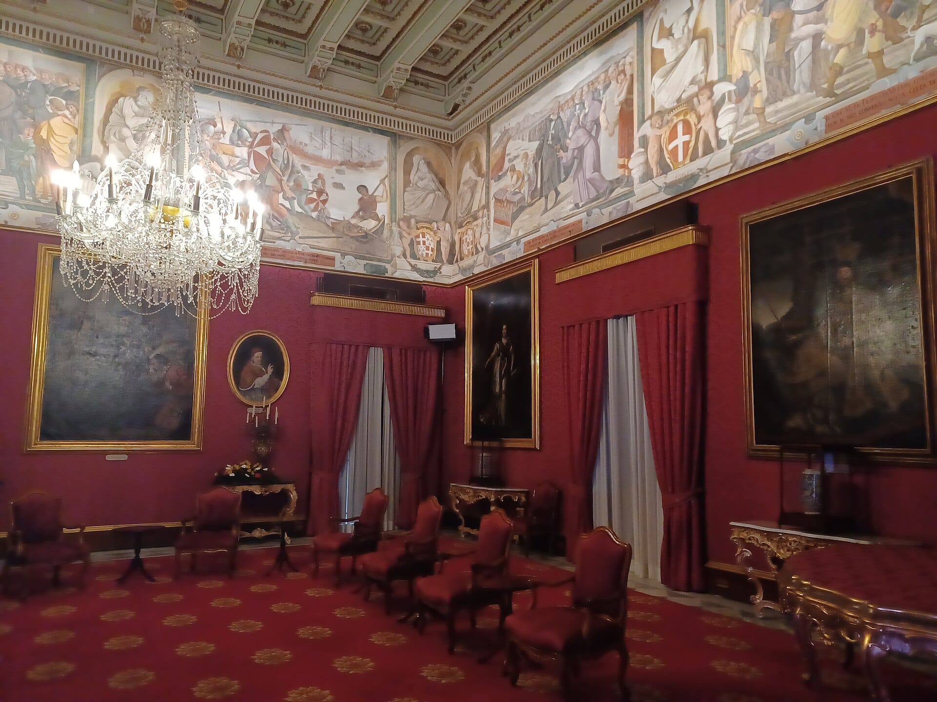 Opulenta Sala di Stato all'interno del Palazzo del Gran Maestro a La Valletta, con elaborati lampadari, tappezzeria rossa, mobili con rifiniture dorate e dipinti storici alle pareti.