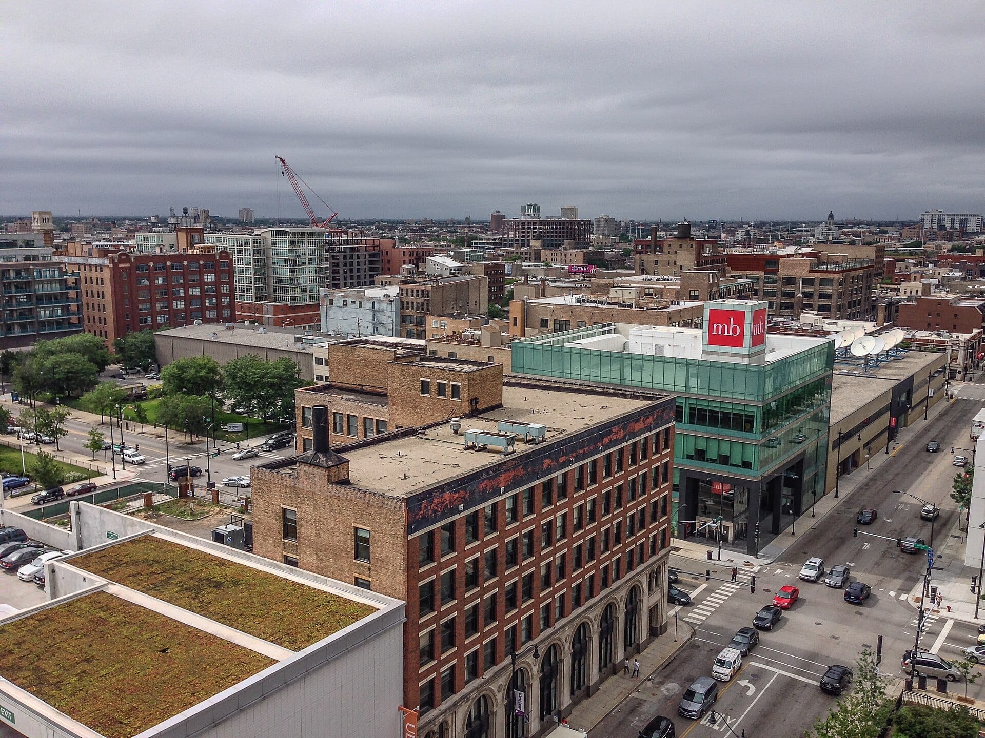 Vista aerea del quartiere Greektown di Chicago e di Halsted Street, con edifici in mattoni, strutture moderne in vetro, traffico stradale e cielo coperto.