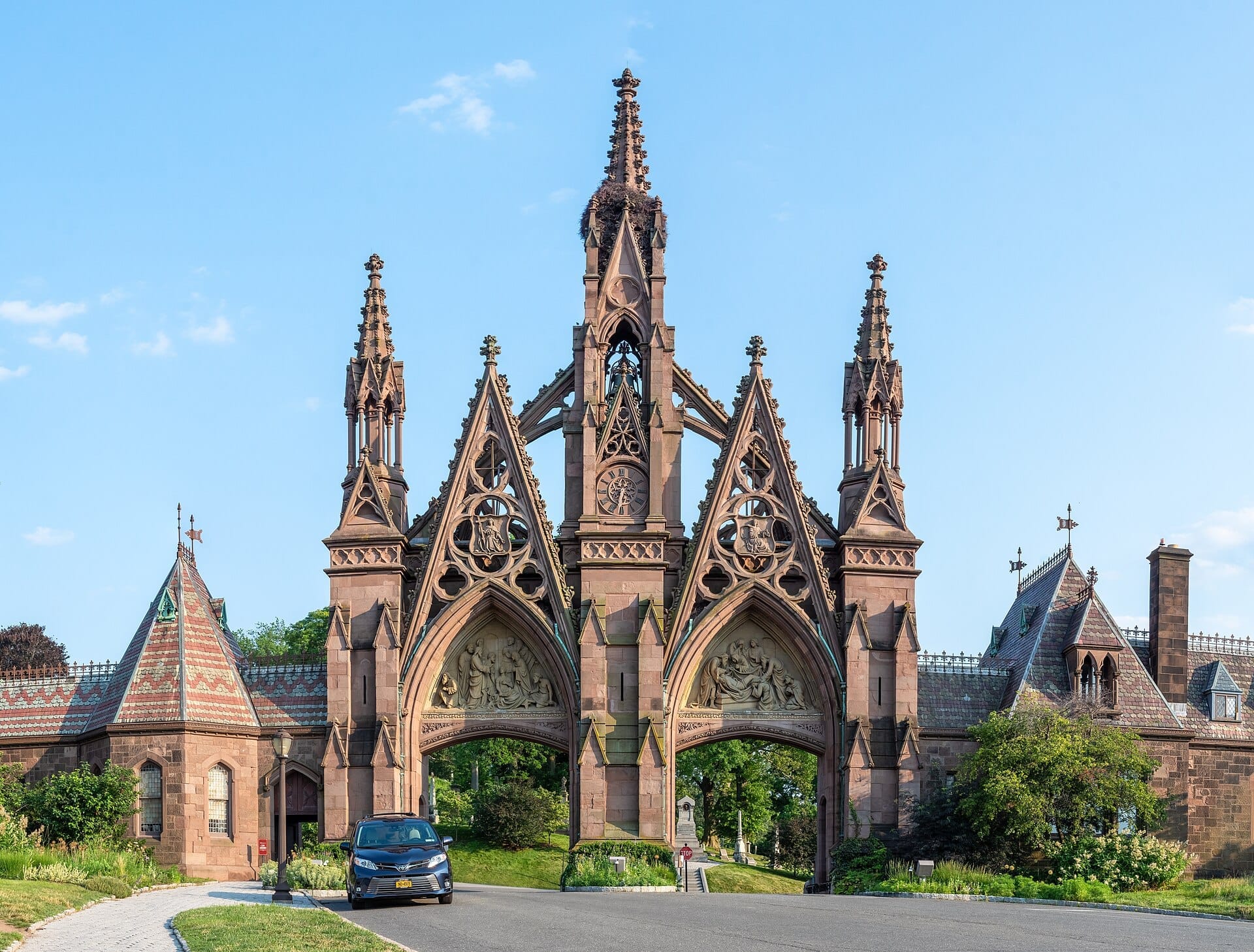 Il sontuoso portale d'ingresso in stile neogotico del Green-Wood Cemetery a Brooklyn, incorniciato da un cielo azzurro limpido e dettagli architettonici.
